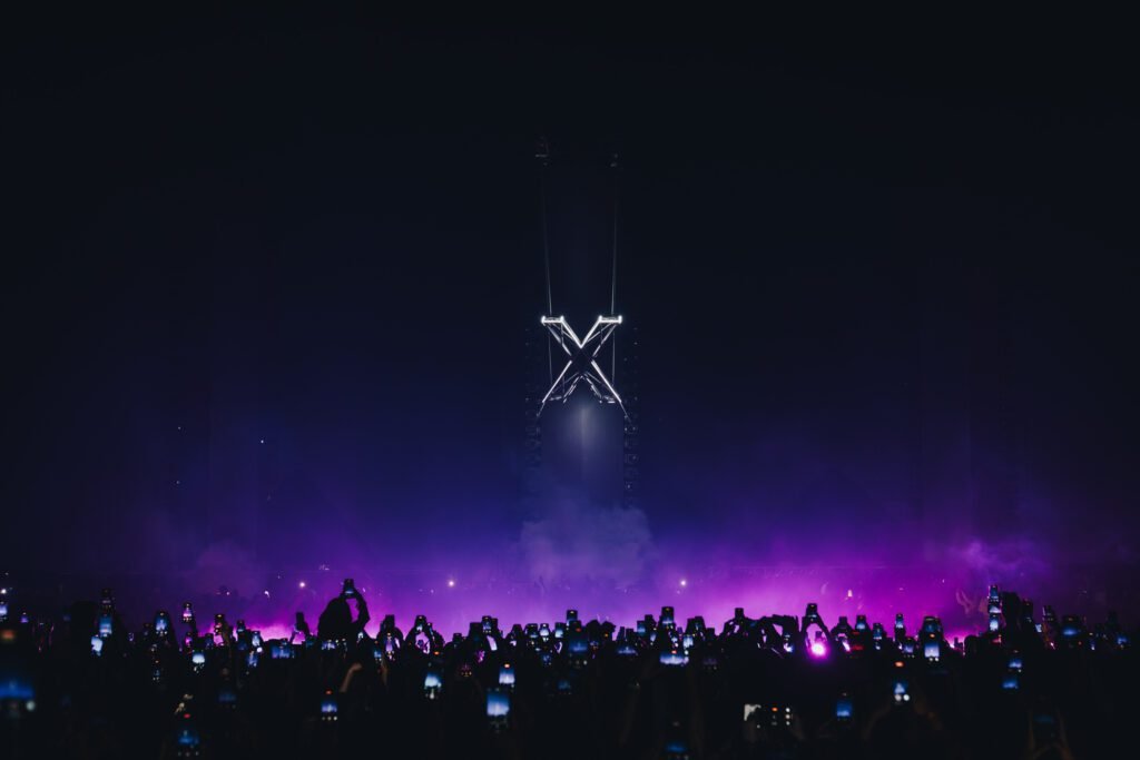 A dupla Adriatique se apresentando no palco do evento 'X' em São Paulo, com o logo do conceito projetado em um grande telão de LED.