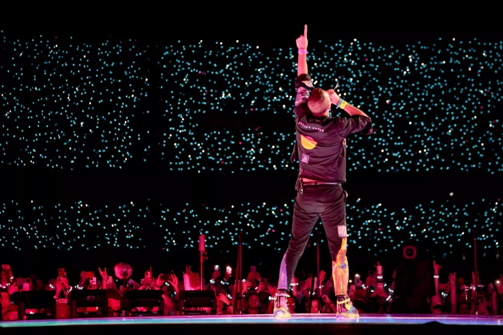 Público com pulseiras de LED coloridas durante show do Coldplay em estádio no Brasil.