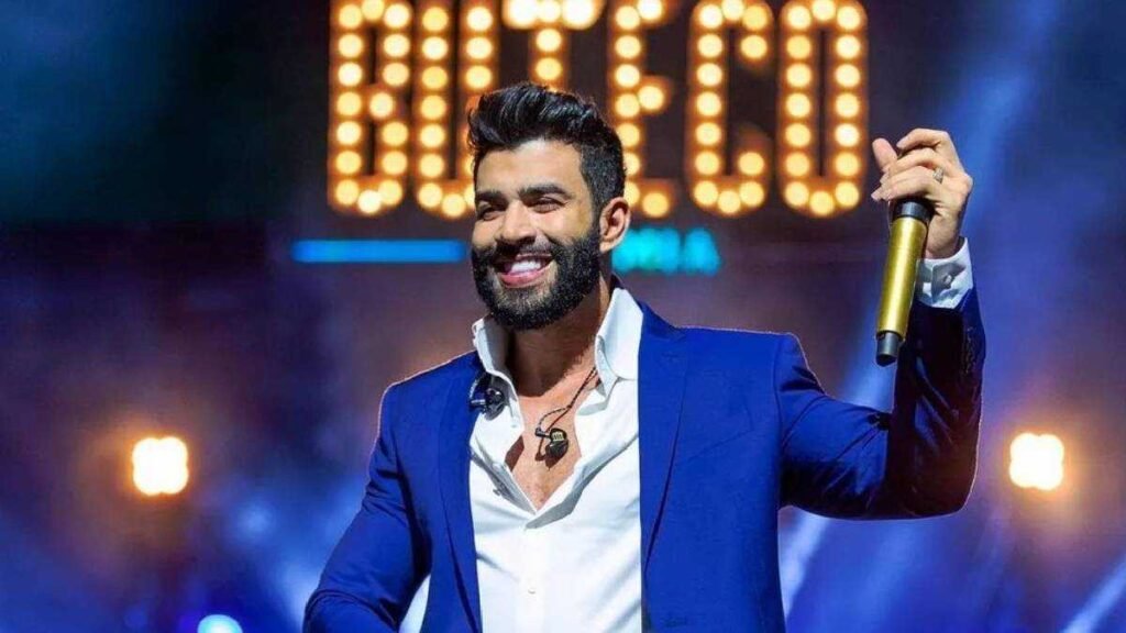 Gusttavo Lima sorrindo no palco com microfone na mão, durante show do Buteco, com o logo do evento iluminado ao fundo.