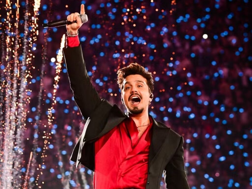 Luan Santana cantando no palco durante a turnê "Registro Histórico" em 2026, com efeitos de luz e multidão ao fundo.