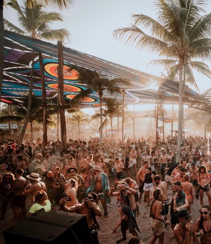 Festival Universo Paralello na Praia de Pratigi em Ituberá, Bahia, com multidão dançando ao som de música eletrônica.